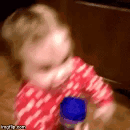 a baby in a red and white polka dot shirt is playing with a blue bottle .