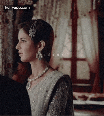 a woman in a white dress and necklace is standing next to a man in a room .