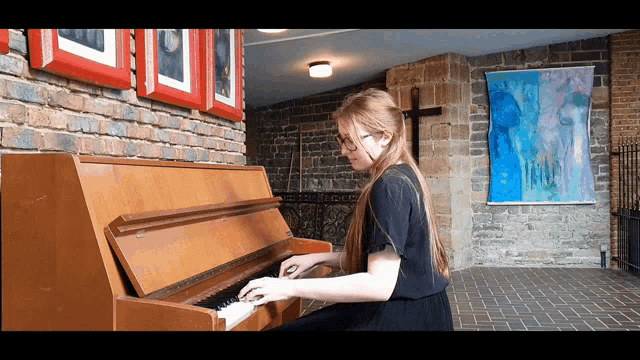 a woman is playing a piano in front of a brick wall and a cross