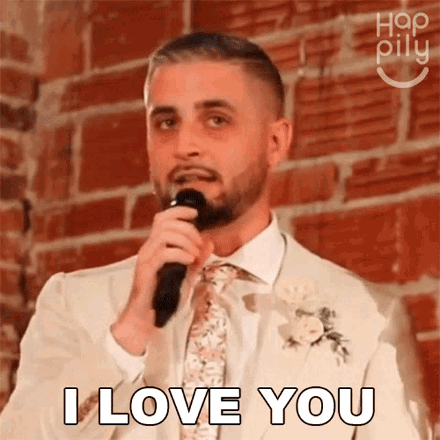 a man in a suit and tie holds a microphone and says i love you