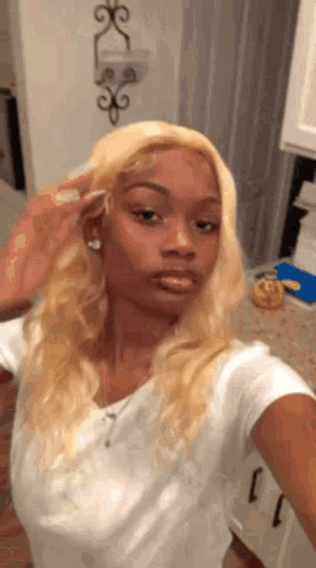 a woman is taking a selfie in a kitchen with her blonde hair .