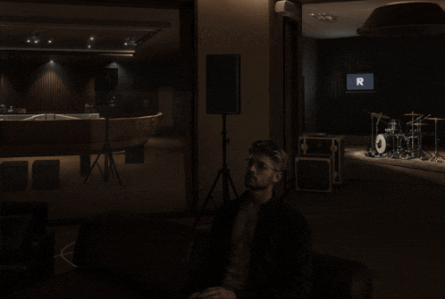 a man sits in a dark room in front of a drum set and a sign that says r
