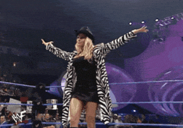 a woman wearing a zebra print coat and cowboy hat stands in a wrestling ring