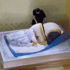 a man in a black shirt is standing next to a bed with a blue blanket