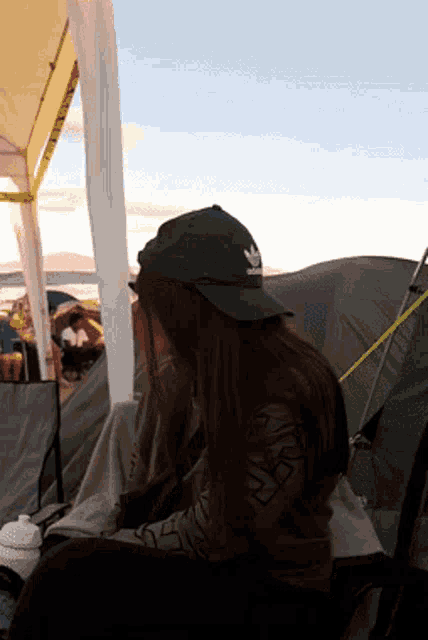 a woman wearing a green adidas hat sits in front of tents