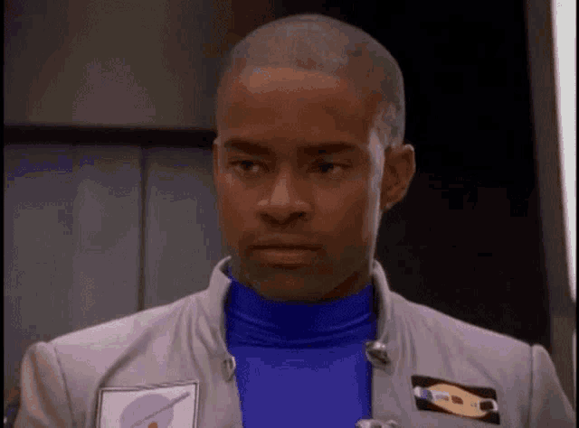 a man in a blue turtleneck and a gray jacket is standing in a room .