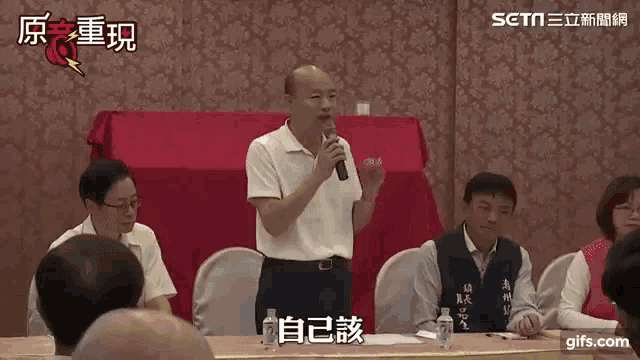 a man is speaking into a microphone in front of a group of people sitting at a table .