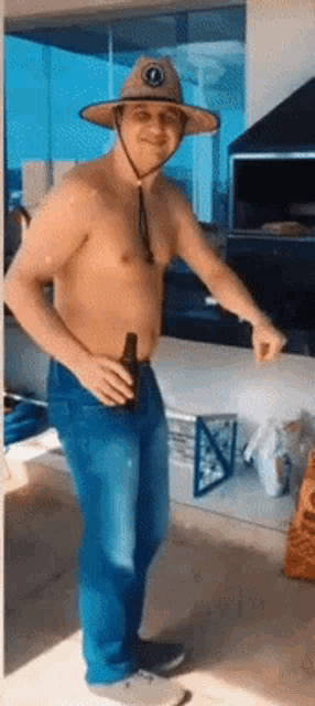 a shirtless man wearing a hat and jeans holds a bottle of beer