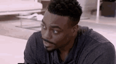 a man with a beard is sitting on the floor in a living room and looking at something .