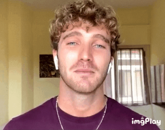 a man with curly hair and a beard is wearing a purple shirt and ear buds .