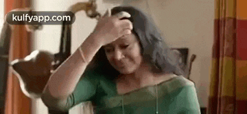 a woman is rubbing her forehead with her hand while wearing a green blouse .