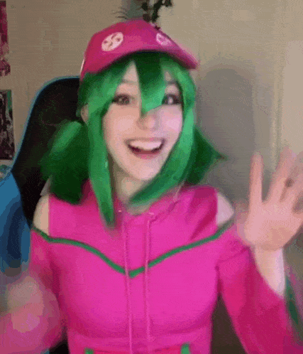 a girl with green hair is wearing a pink hoodie and a hat .