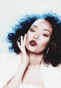a woman with curly hair is wearing hoop earrings and red lips