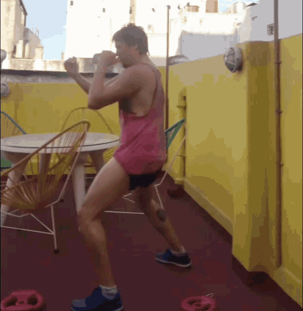 a man in a pink tank top is standing on a patio