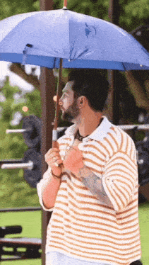 a man in a striped shirt is holding an umbrella in the rain .