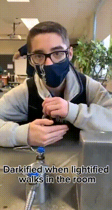 a young man wearing a mask and glasses is sitting at a table with a bottle in his hand .