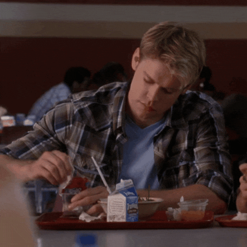 a man in a plaid shirt is sitting at a table with a tray of food and a carton of johnson 's milk
