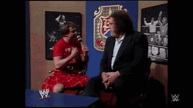 a man in a red kilt is fighting another man in a suit in front of a wwe logo