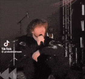 a man with curly hair is singing into a microphone on stage