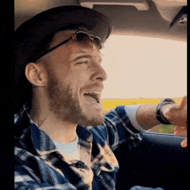 a man wearing sunglasses and a plaid shirt is singing in the car