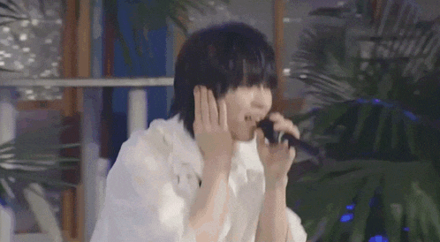 a man in a white shirt is singing into a microphone in front of a palm tree .