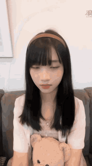 a girl sitting on a couch holding a teddy bear with her eyes closed