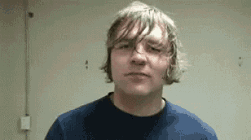 a man with long hair is wearing a blue shirt and making a funny face