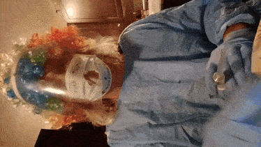 a woman in a clown costume wearing a face shield and gloves holds a bottle of alcohol