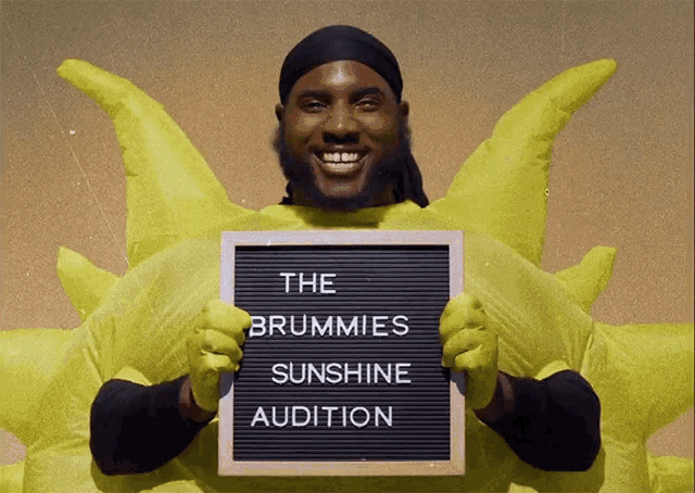 a man in a sun costume is holding a sign that says " the brummies sunshine audition "