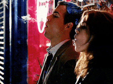 a man and a woman are smoking cigarettes in front of a window