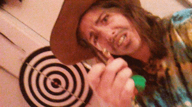 a man in a cowboy hat is holding a green object in front of a target