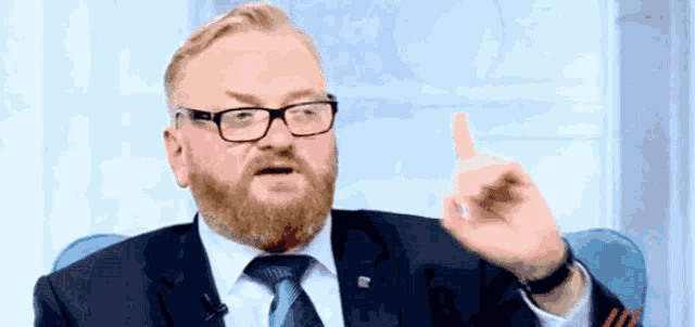 a man with a beard wearing glasses and a tie is pointing up