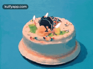 a birthday cake with candles and sprinkles on a blue surface .