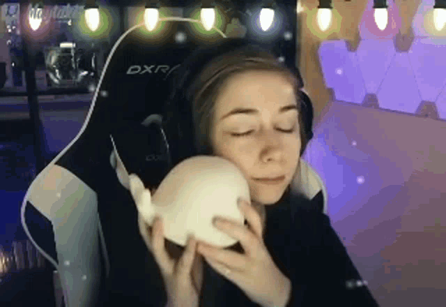 a woman is sitting in a gaming chair holding a stuffed animal in front of her face .