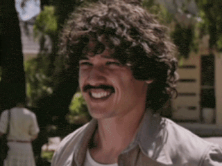 a man with curly hair and a mustache is smiling and laughing .