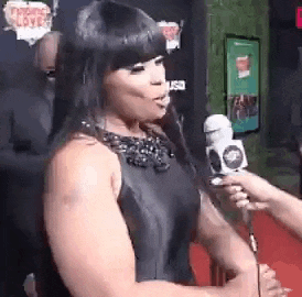 a woman is being interviewed by a reporter on a red carpet while holding a microphone .
