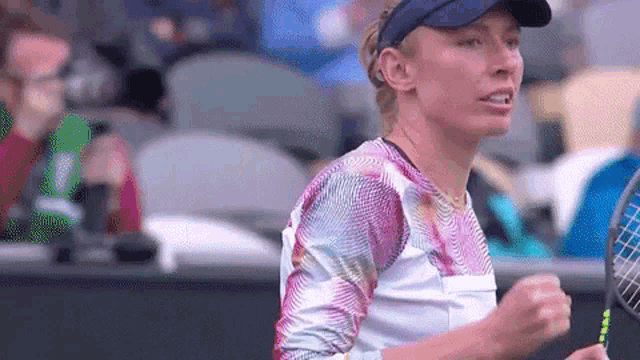 a woman is holding a tennis racquet on a tennis court while wearing a visor .