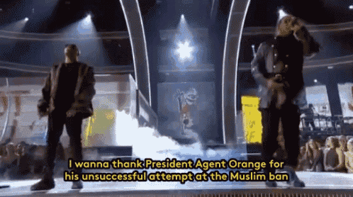 two men standing on a stage with the words " i wanna thank president agent orange for his unsuccessful attempt at the muslim ban "
