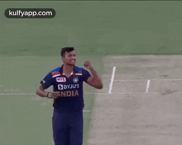 a cricket player in a blue jersey is standing on a field .
