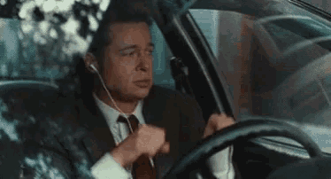 a man in a suit and tie is sitting in a car wearing ear buds .