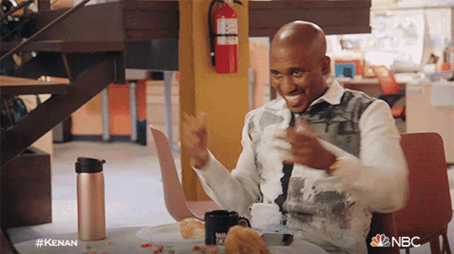 a man is sitting at a table with a plate of food and a nbc logo on the table