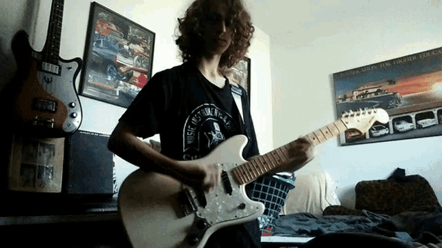a man playing a guitar in a room with a poster on the wall that says fast and furious