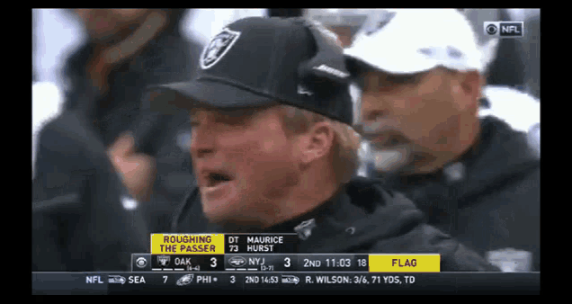 a man wearing a raiders hat watches a game