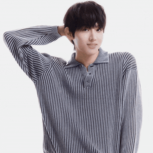 a young man wearing a striped sweater holds his hand to his head