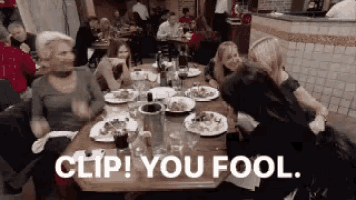 a group of people are sitting at a table with plates of food and a sign that says clip you fool ..