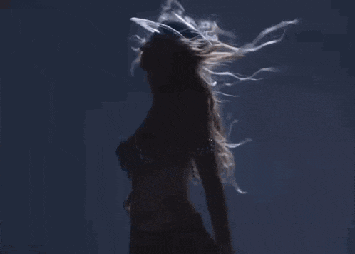 a woman is dancing with her hair blowing in the wind while wearing a bra .