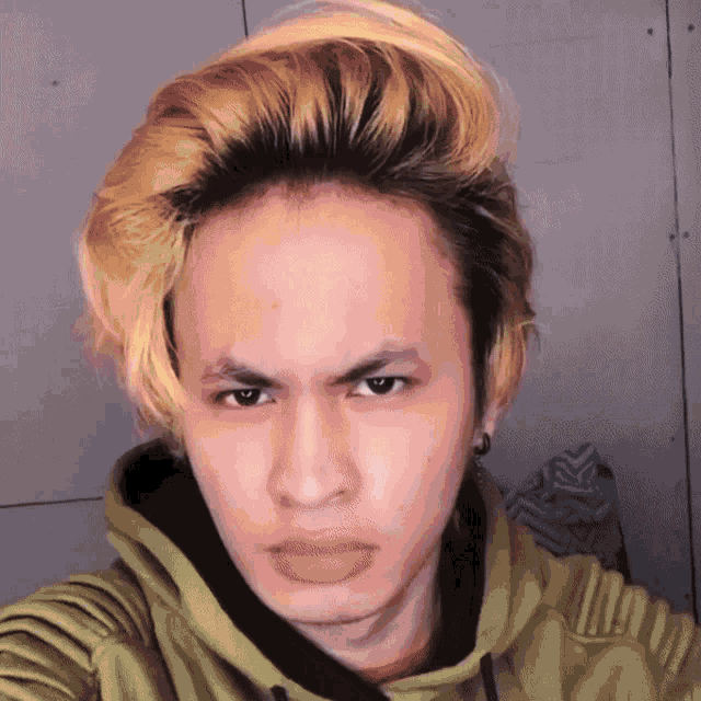 a young man with blonde hair and a green hoodie looks at the camera