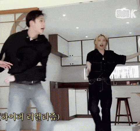 a man and a woman are dancing in a kitchen with a studio k sign above them