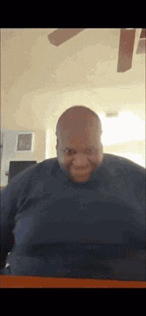a bald man is smiling in front of a ceiling fan in a living room
