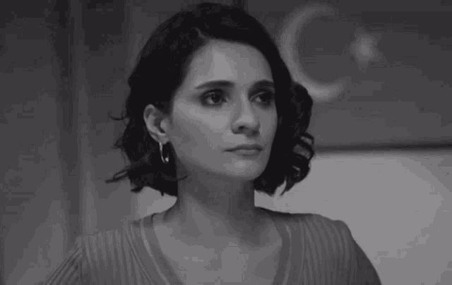 a black and white photo of a woman in a sweater looking at the camera .